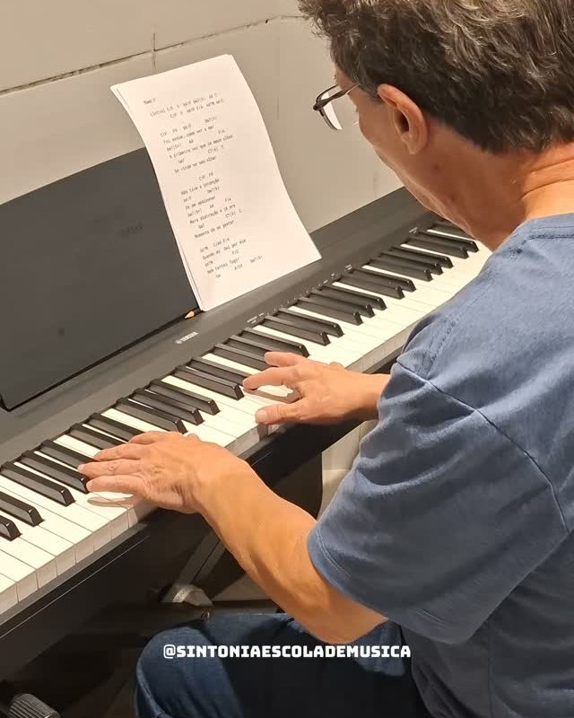 Professor tocando piano com a partitura na estante