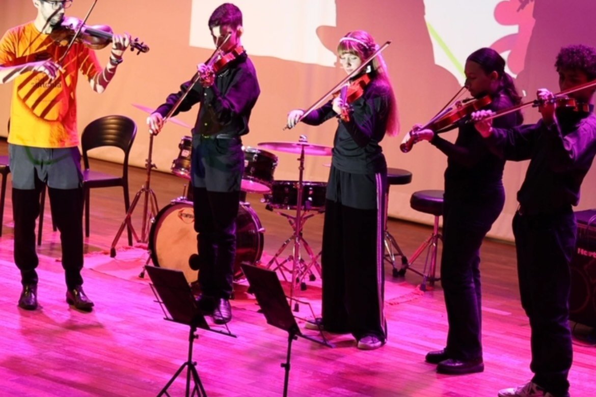Alunos de violino tocando no palco do Teatro Carolina Maria de Jesus, no CEU Carrão